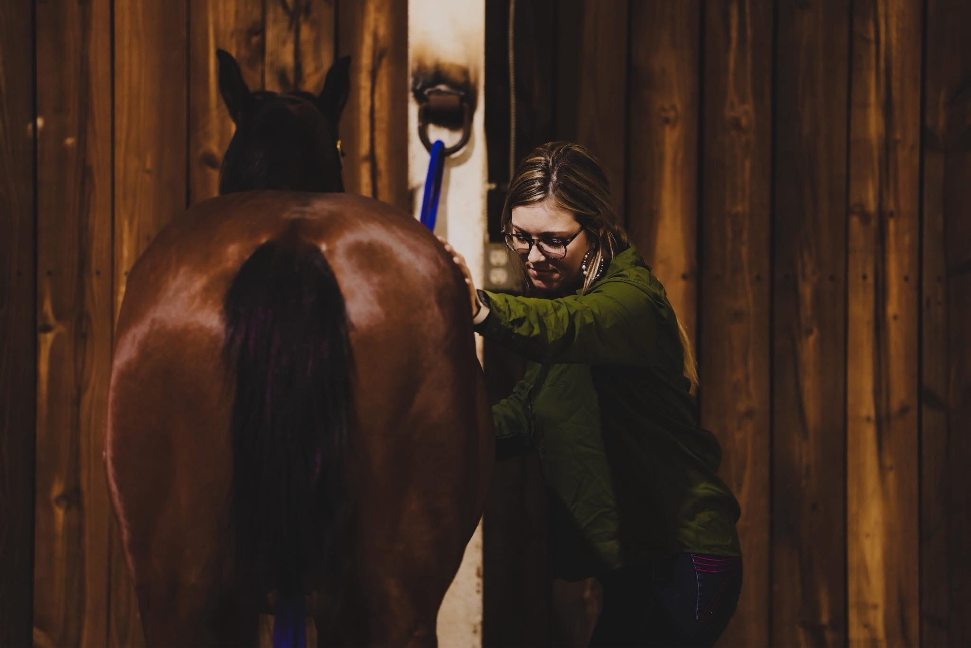 Madison grooming her horse in a warm-lit stable
