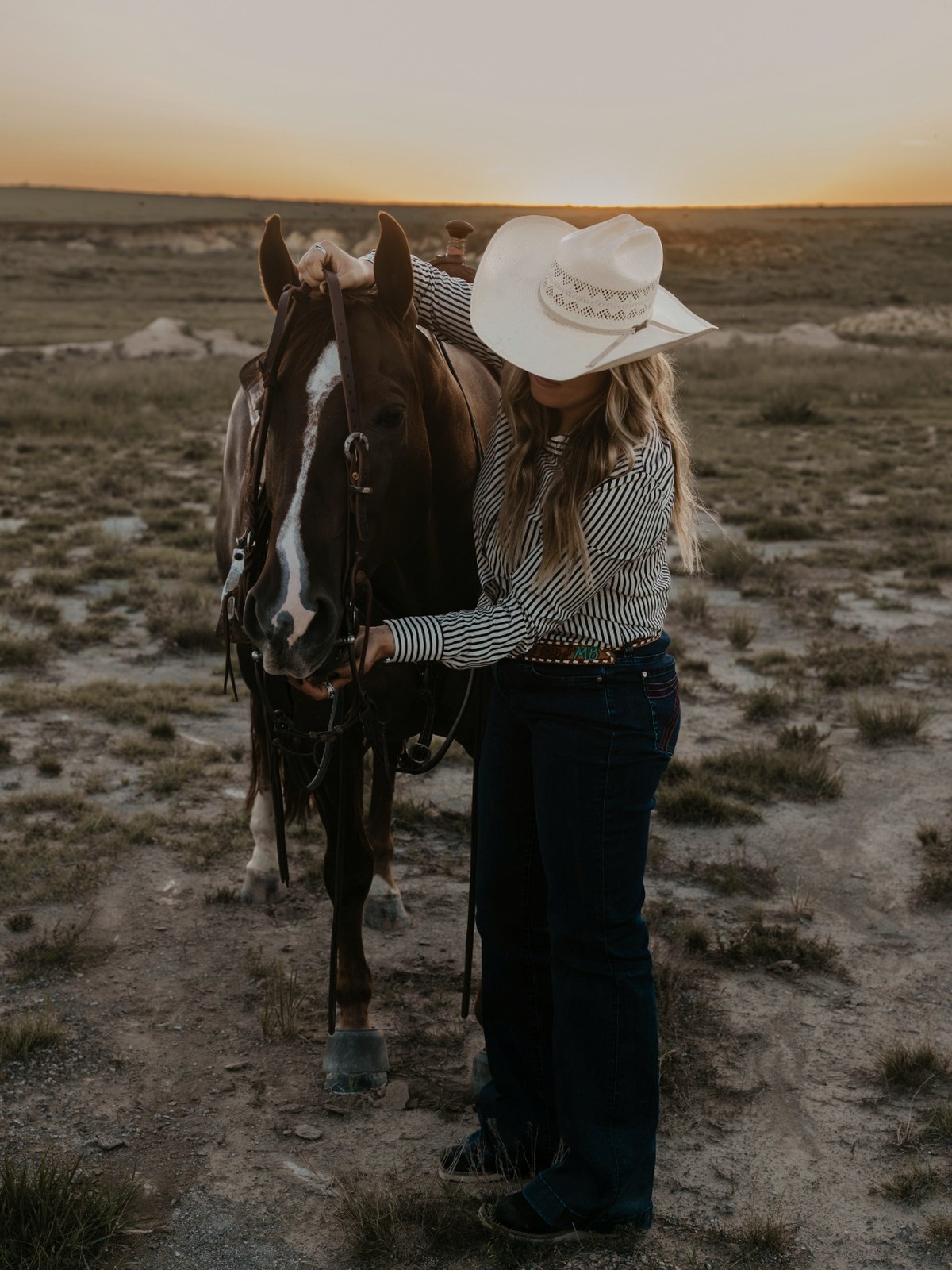 Madison bridling her horse on open prairie at sunset